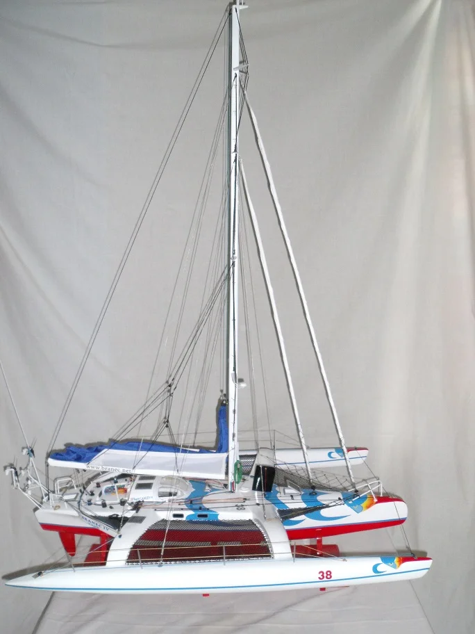 High-end handcrafted wooden scale model of a modern racing trimaran yacht with three hulls and full sails on a display stand.